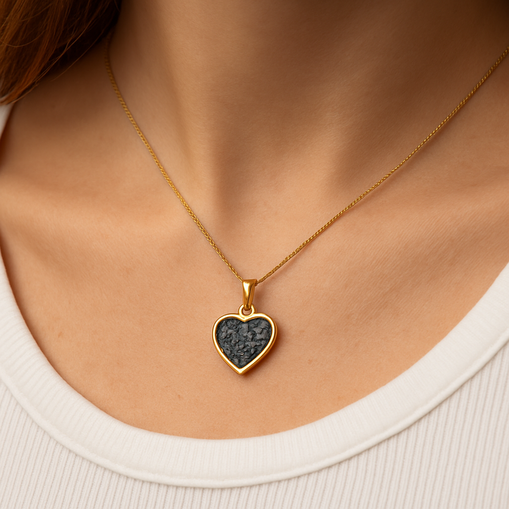 Gold heart-shaped necklace with a dark green stone on a person wearing a white top.